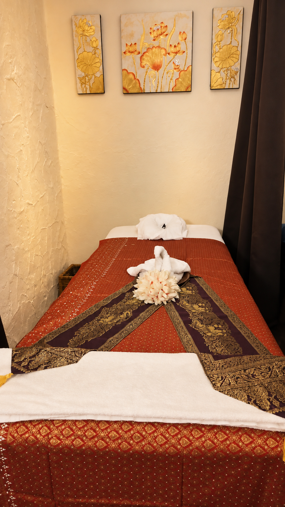 Liebevoll vorbereitete Massageliege mit rot-goldenen Textilien und Lotusbildern